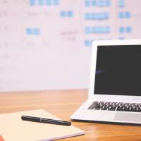 Apple macbook air turned off next to notepad and pen in front of white board